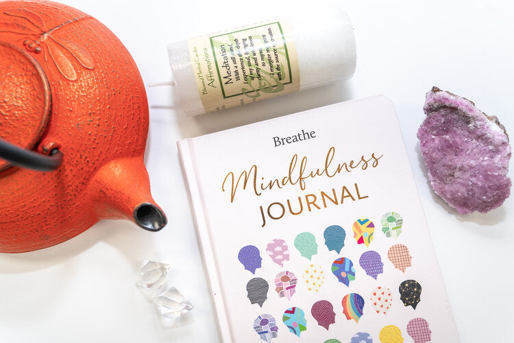 mindfulness journal, candle, stone and red tea pot layer out on a white table