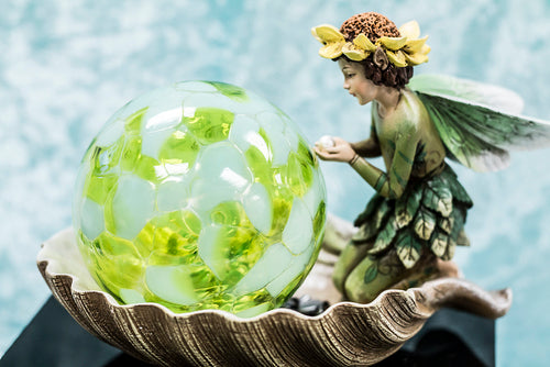 fairy girl kneeling beside green crystal/glass ball